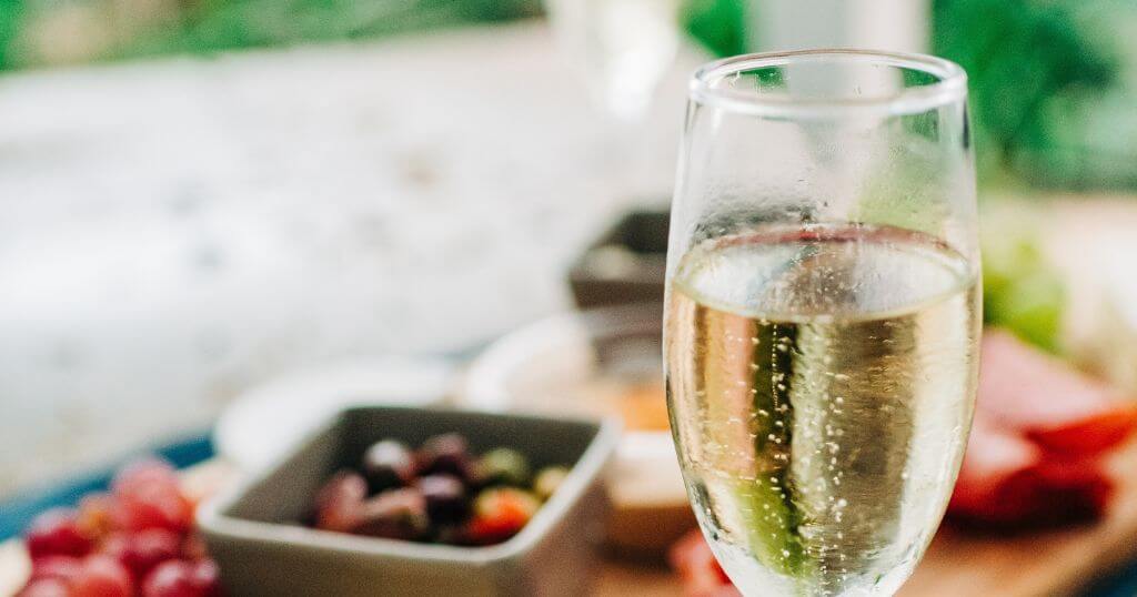 foto contém uma taça de vinho branco ao lado de tipos de queijos