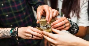 Foto mostra uma brinde com doses de cachaça entre jovens