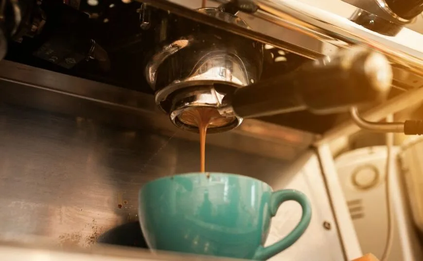 Foto mostra caneca abaixo de uma saída de maquina de café