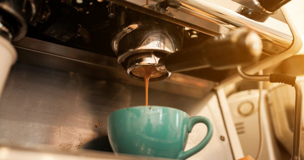 Foto mostra caneca abaixo de uma saída de maquina de café